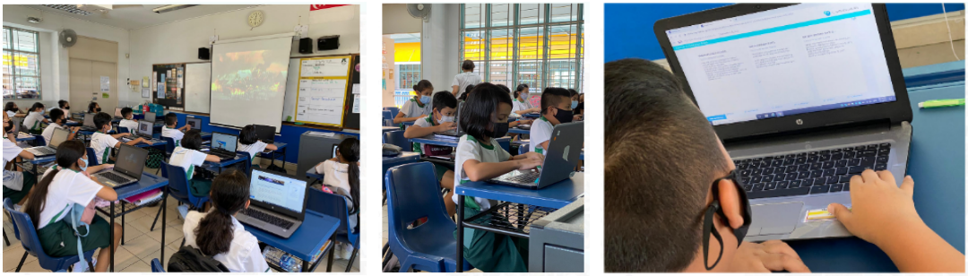 Students in a classroom wearing masks use laptops, with a projected whiteboard visible at the front.